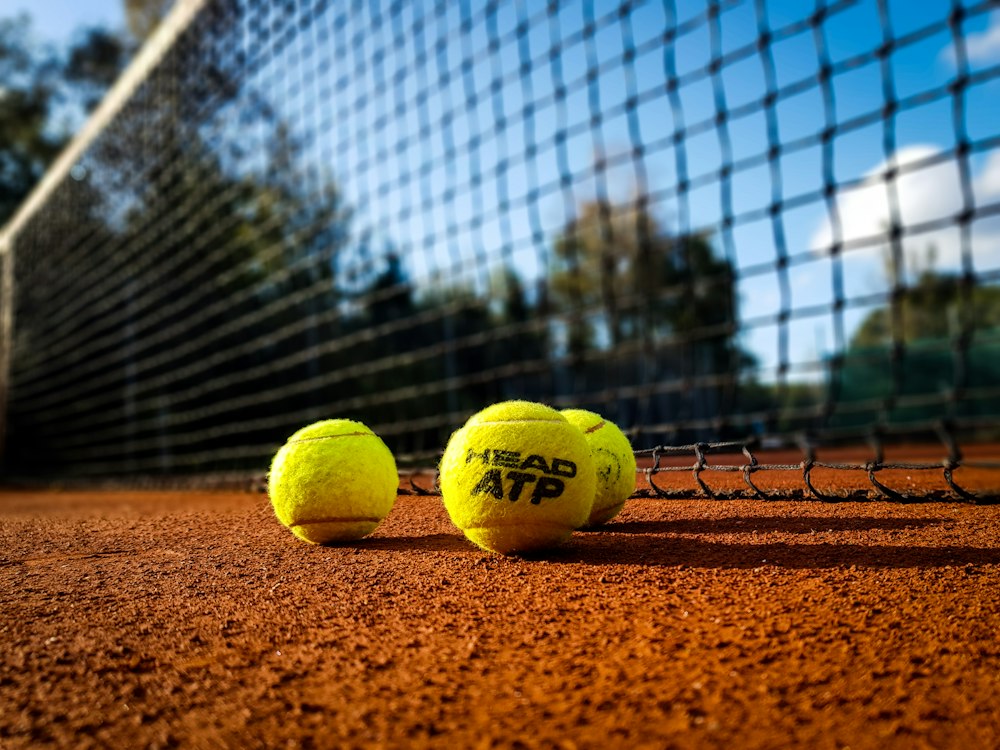 pelota de tenis amarilla sobre arena marrón